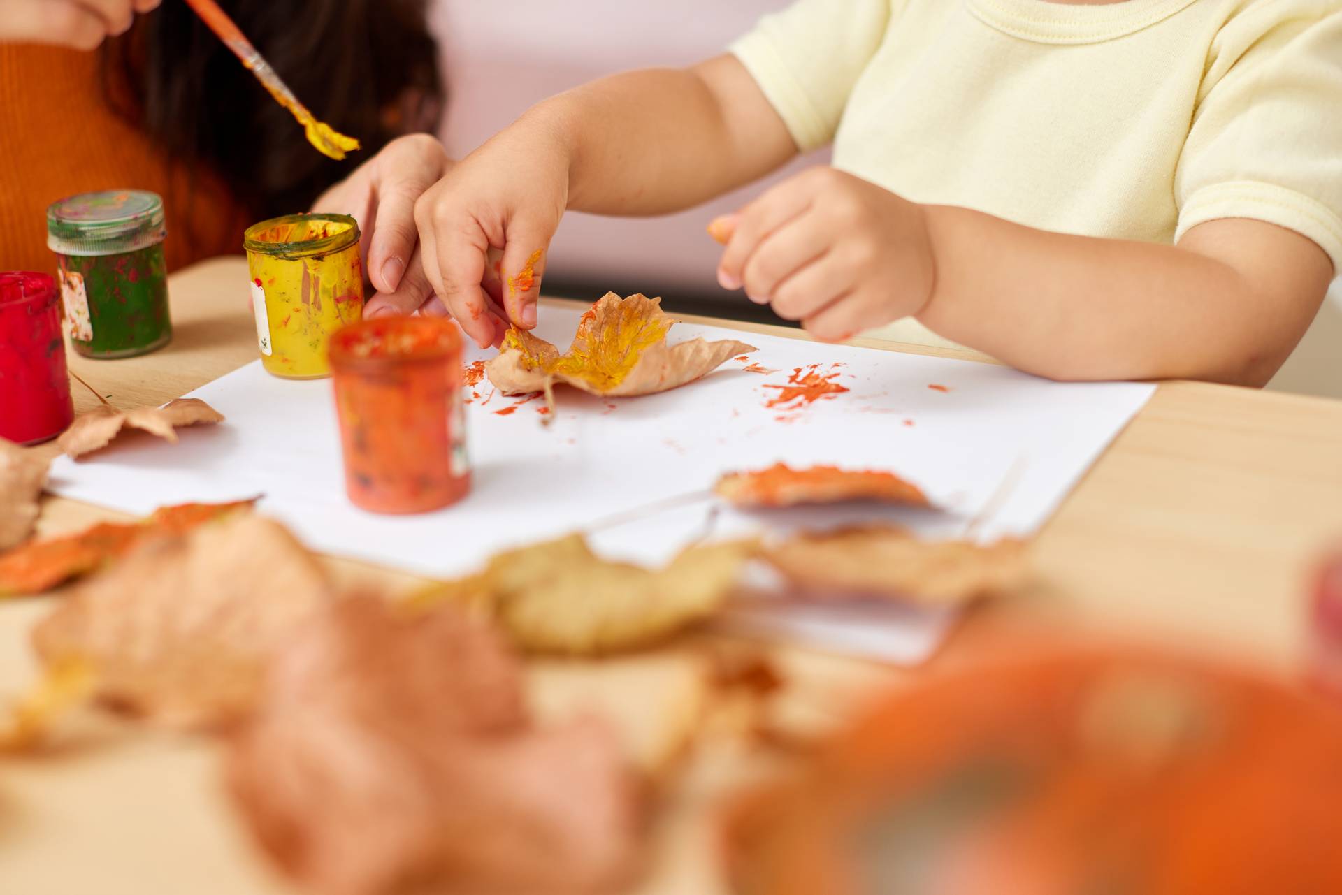 close-up, child and mom hands painting autumn yellow leaves together. happy time together at home