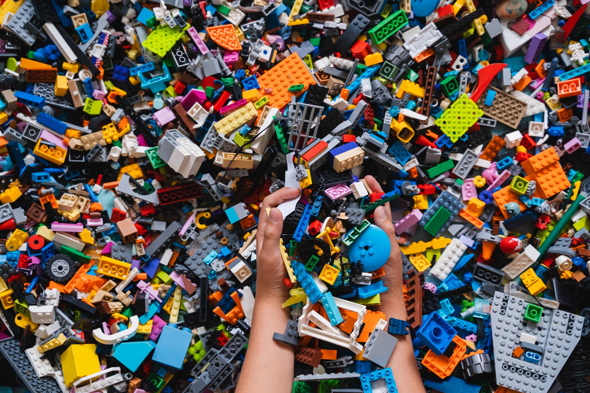 Huge pile of mixed colorful plastic bricks toys with children's hands. Small plastic building blocks in multiple colours, top view, lifestyle photo. Kids leisure, children education and development.